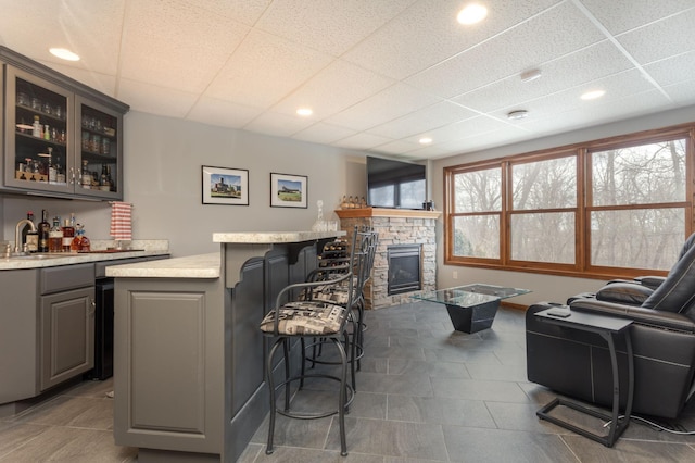 living room with wet bar, a stone fireplace, and a paneled ceiling