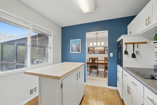 kitchen with visible vents, stainless steel oven, a center island, a chandelier, and white cabinets