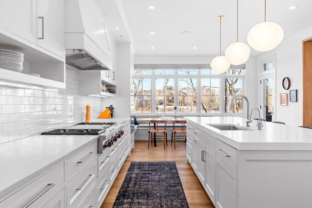 kitchen featuring a sink, custom exhaust hood, open shelves, light countertops, and light wood-style floors