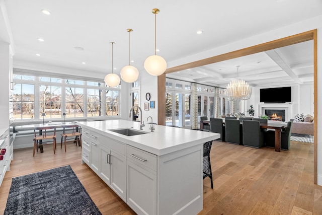 kitchen with a sink, light wood-type flooring, light countertops, a warm lit fireplace, and beam ceiling