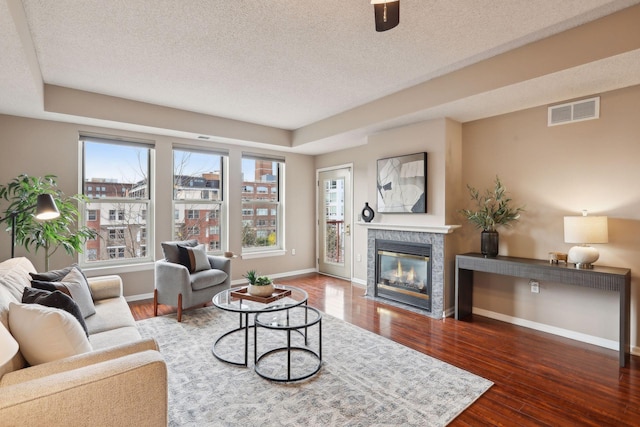 living area with wood finished floors, a textured ceiling, a tiled fireplace, baseboards, and visible vents