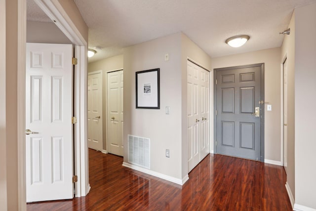 foyer entrance with baseboards, wood finished floors, visible vents, and a textured ceiling