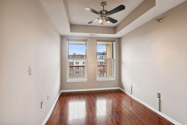 unfurnished room featuring a ceiling fan, baseboards, a raised ceiling, and wood-type flooring