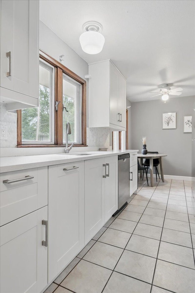 kitchen with stainless steel dishwasher, tasteful backsplash, light countertops, light tile patterned flooring, and white cabinets