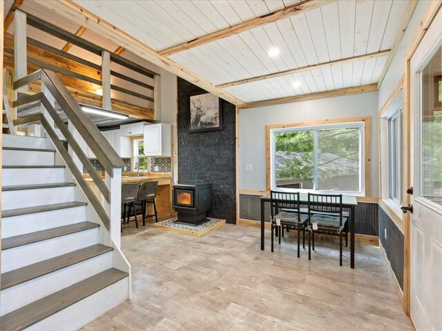 6274 Azalea Rd, Motley Twp, MN 56466 - dining space featuring wood ceiling with exposed beams, a wood stove, light wood-style floors, stairs, and a wainscoted wall