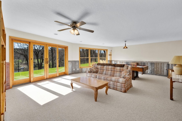 carpeted living area featuring a ceiling fan, a textured ceiling, and a wainscoted wall