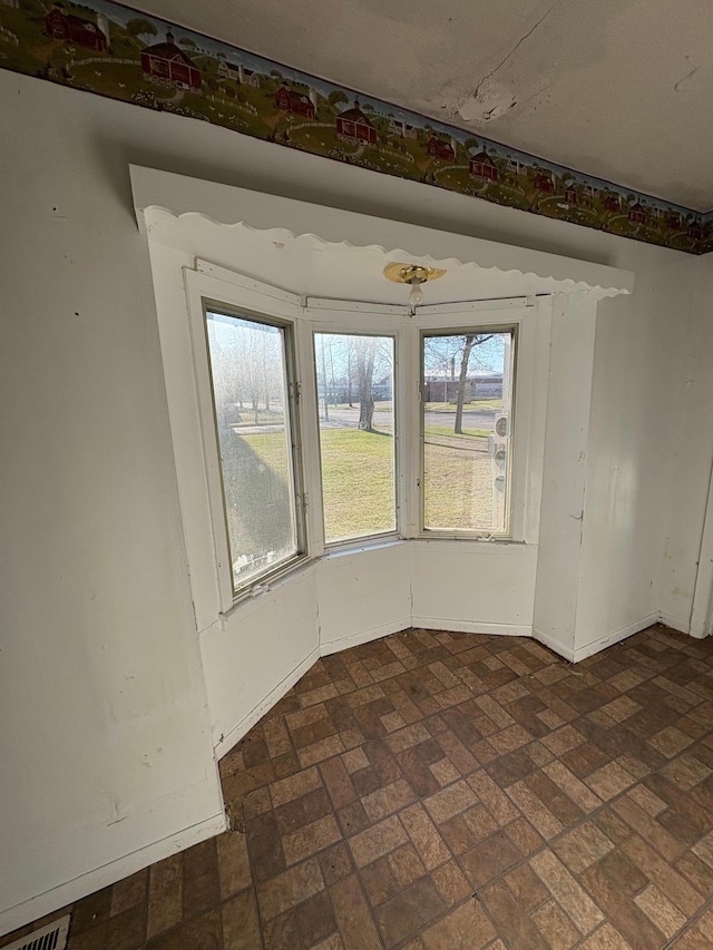 unfurnished room with brick patterned floor, baseboards, and visible vents