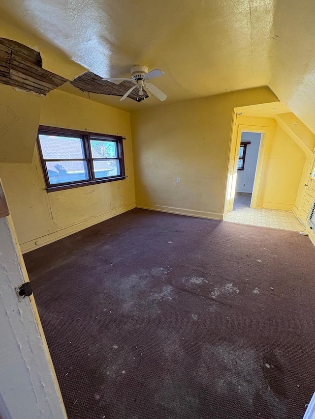 spare room featuring a textured ceiling, baseboards, carpet flooring, ceiling fan, and vaulted ceiling