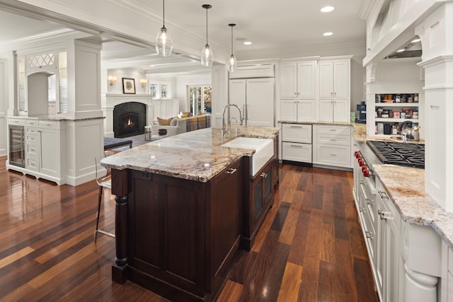 4812 Maple Rd, Edina, MN 55424 - kitchen with a kitchen island with sink, a sink, wine cooler, dark wood finished floors, and a warm lit fireplace