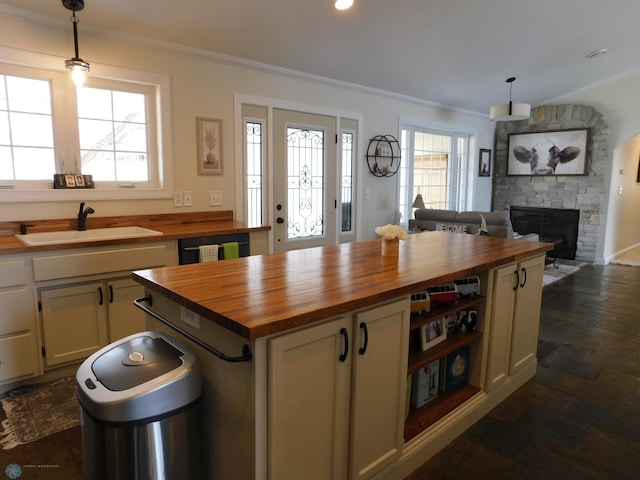 kitchen featuring ornamental molding, wooden counters, a stone fireplace, and a sink