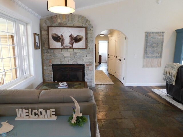 living room with stone tile flooring, crown molding, arched walkways, plenty of natural light, and baseboards