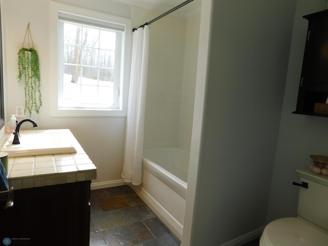 full bath featuring toilet, shower / bath combo with shower curtain, stone tile flooring, baseboards, and vanity