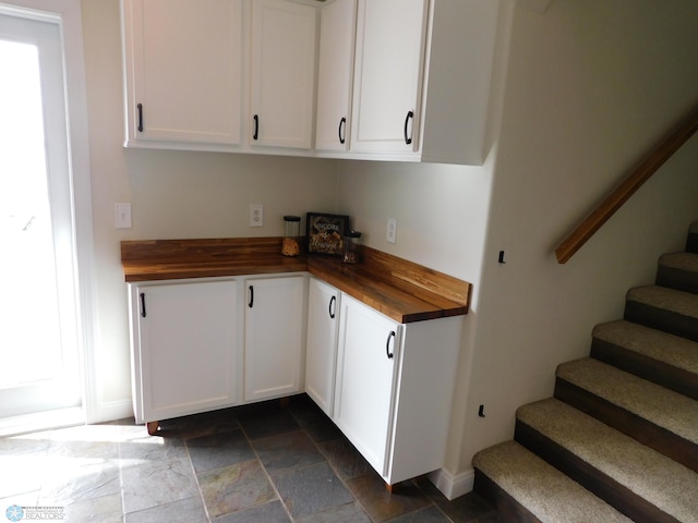 kitchen with baseboards, butcher block countertops, stone tile floors, and white cabinets