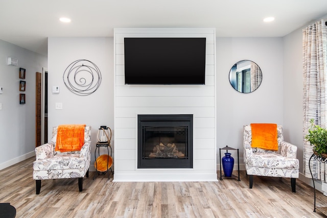 sitting room with baseboards, recessed lighting, wood finished floors, and a large fireplace