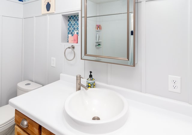 bathroom with toilet, a decorative wall, and vanity