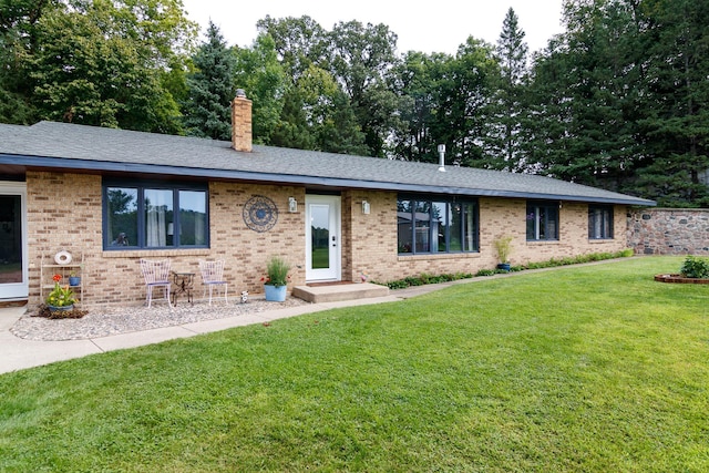 ranch-style home with a front yard, a shingled roof, brick siding, and a chimney