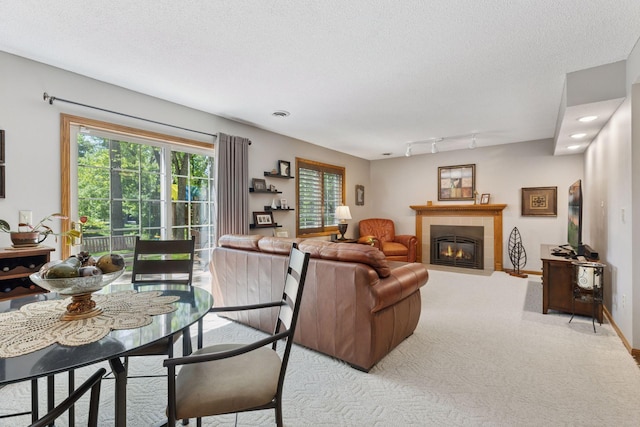living room with carpet floors, a tiled fireplace, a textured ceiling, track lighting, and baseboards
