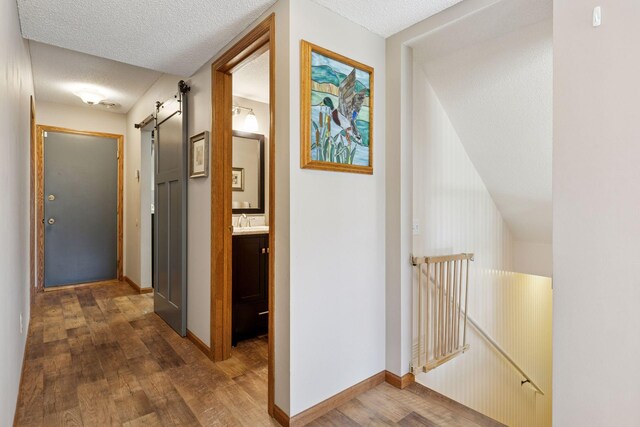 hall with dark wood-style floors, a barn door, baseboards, a textured ceiling, and a sink