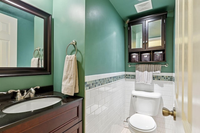 half bath with tile walls, toilet, wainscoting, and vanity