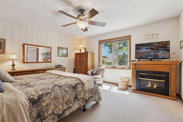 bedroom featuring carpet, baseboards, a glass covered fireplace, a textured ceiling, and a ceiling fan