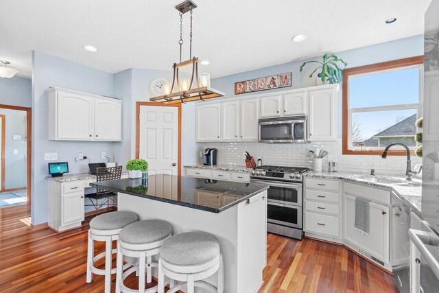 kitchen with a sink, wood finished floors, white cabinets, and stainless steel appliances