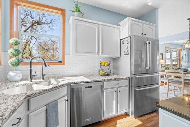 kitchen featuring light wood-type flooring, white cabinetry, light stone counters, a sink, and appliances with stainless steel finishes