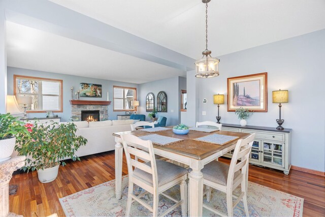 dining area with an inviting chandelier, dark wood-style flooring, baseboards, and a stone fireplace