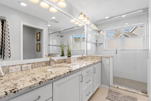 bathroom featuring double vanity, a textured ceiling, a shower stall, a sink, and tile patterned floors