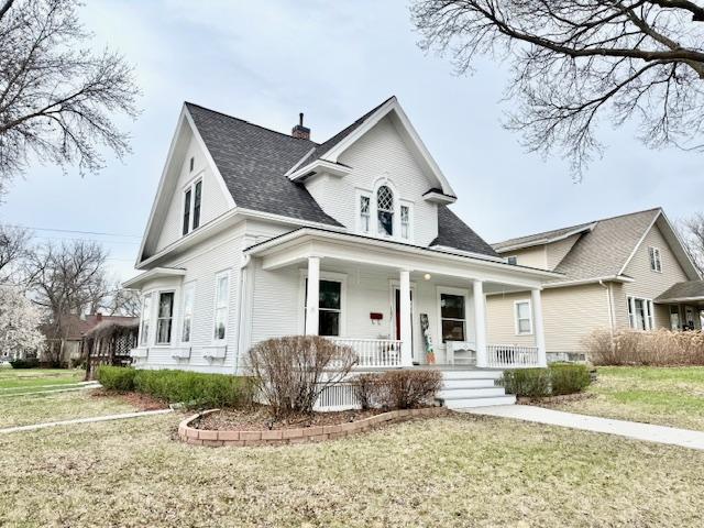 bungalow-style home with a shingled roof, a porch, a front lawn, and a chimney
