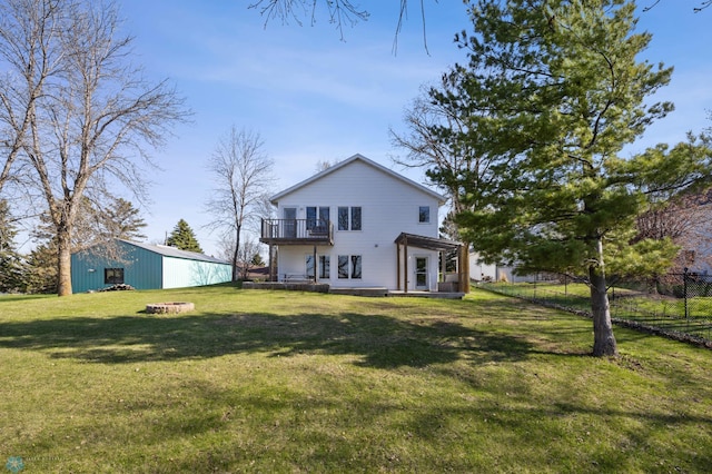 rear view of property featuring a balcony, a yard, an outbuilding, and fence