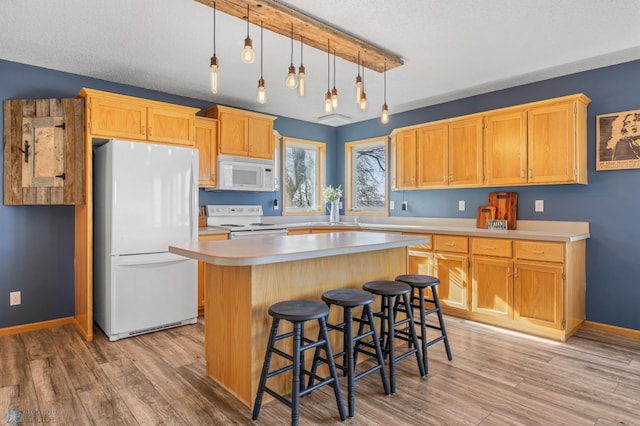 kitchen with light wood finished floors, light countertops, a kitchen island, and white appliances