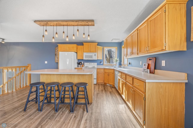 kitchen with a kitchen bar, white appliances, light countertops, light wood-style floors, and a kitchen island