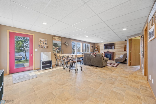 living area featuring a paneled ceiling, plenty of natural light, stone finish floor, and a glass covered fireplace