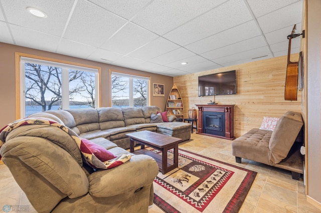 living room featuring a paneled ceiling, wood walls, a glass covered fireplace, and recessed lighting
