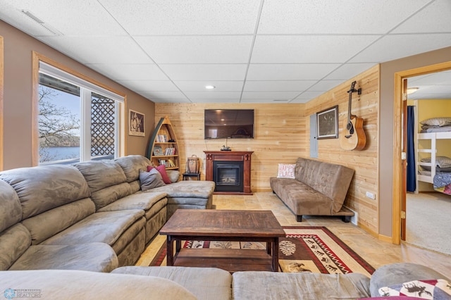 living area featuring a drop ceiling, recessed lighting, a glass covered fireplace, visible vents, and wooden walls