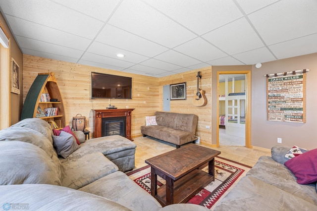 living area featuring recessed lighting, baseboards, a glass covered fireplace, wooden walls, and a paneled ceiling