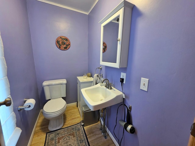 half bath featuring wood finished floors, toilet, baseboards, ornamental molding, and a sink