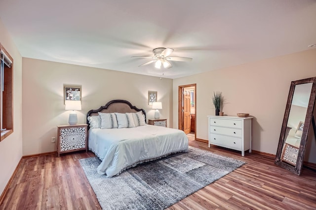 bedroom with baseboards, ceiling fan, ensuite bath, and wood finished floors