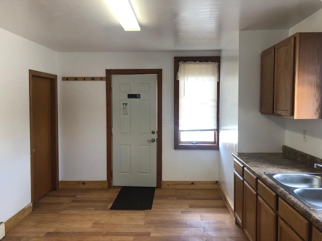 kitchen with brown cabinets, dark countertops, a sink, light wood-style floors, and baseboards