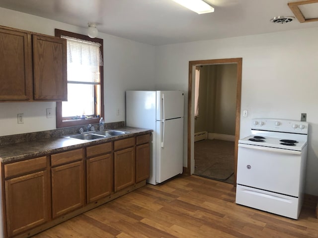 kitchen with dark countertops, a sink, white appliances, light wood finished floors, and visible vents