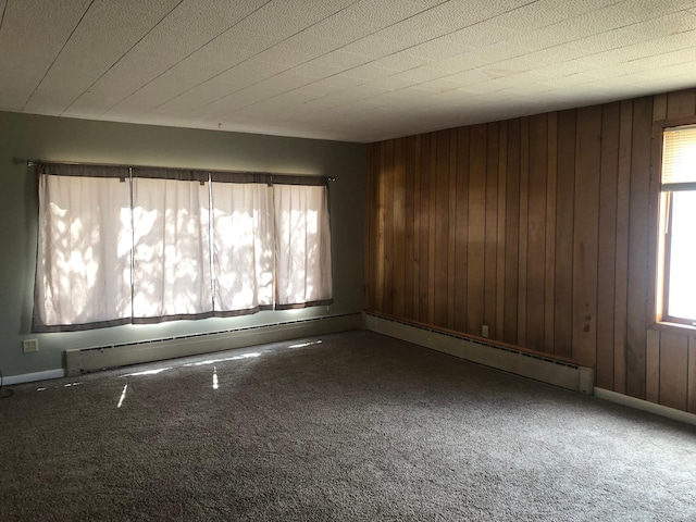 empty room featuring a baseboard heating unit, wood walls, and carpet flooring