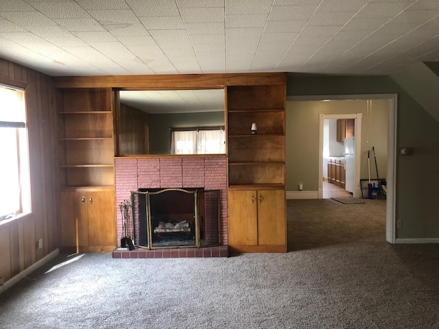 unfurnished living room featuring carpet floors, a healthy amount of sunlight, a tile fireplace, and wooden walls