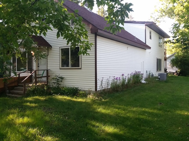 view of side of home featuring a lawn, cooling unit, and roof with shingles