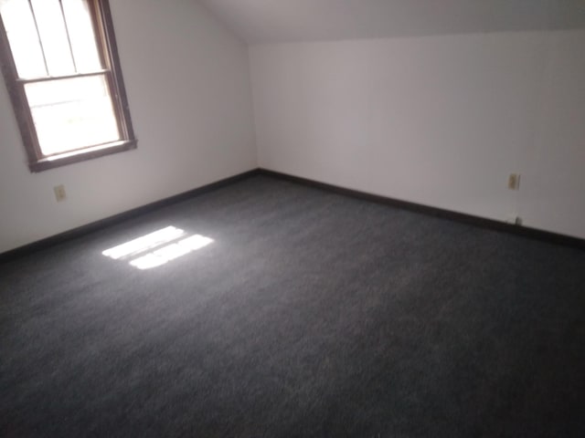 additional living space with dark carpet, baseboards, and lofted ceiling