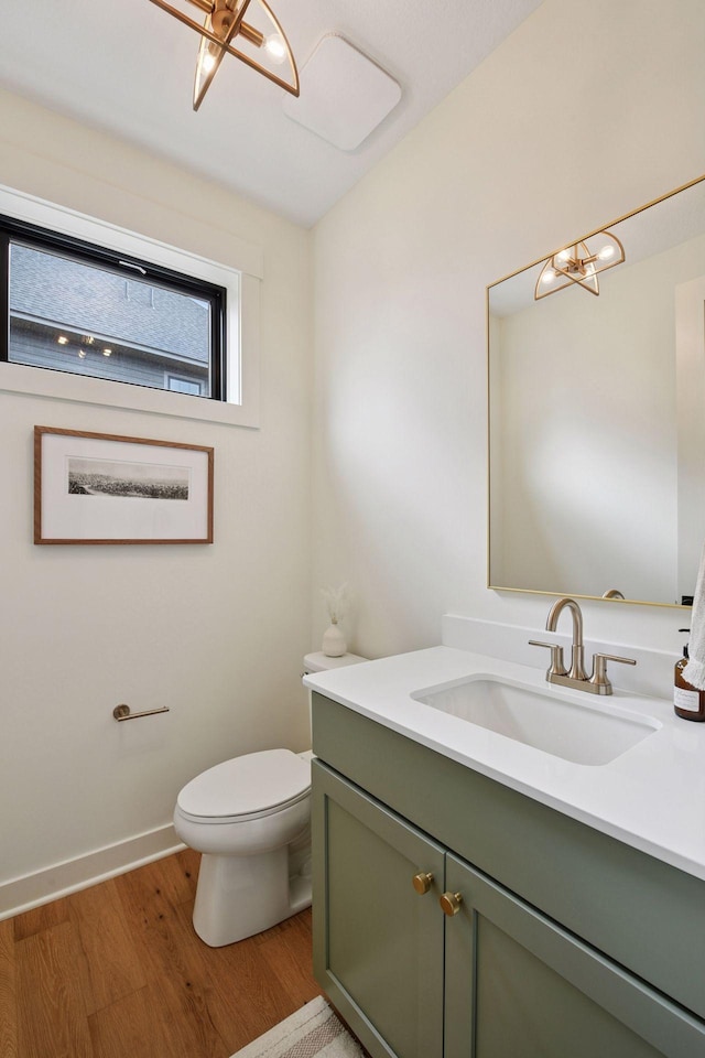 half bathroom with an inviting chandelier, wood finished floors, toilet, vanity, and baseboards