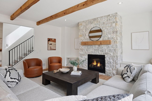 living area with a stone fireplace, wood finished floors, stairs, and beamed ceiling