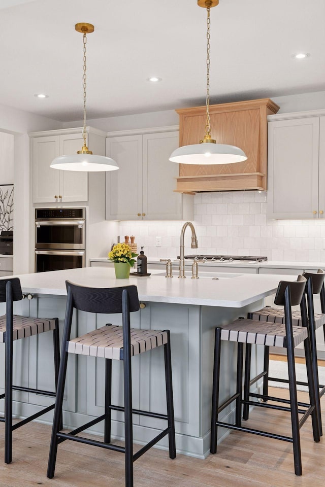 kitchen featuring backsplash, stainless steel appliances, light wood finished floors, and light countertops