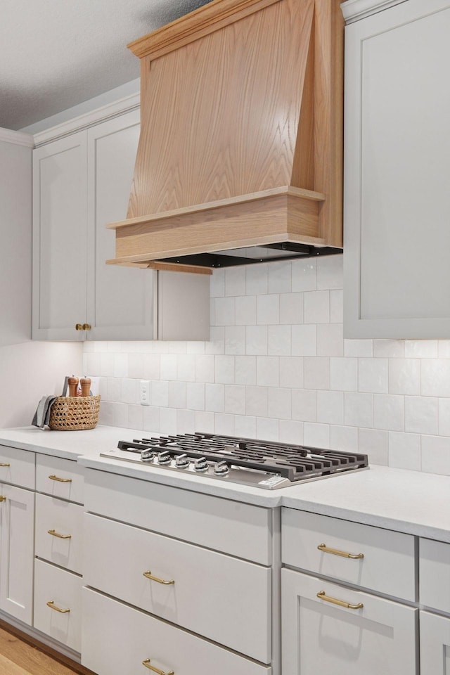 kitchen featuring custom exhaust hood, backsplash, white cabinetry, stainless steel gas stovetop, and light countertops
