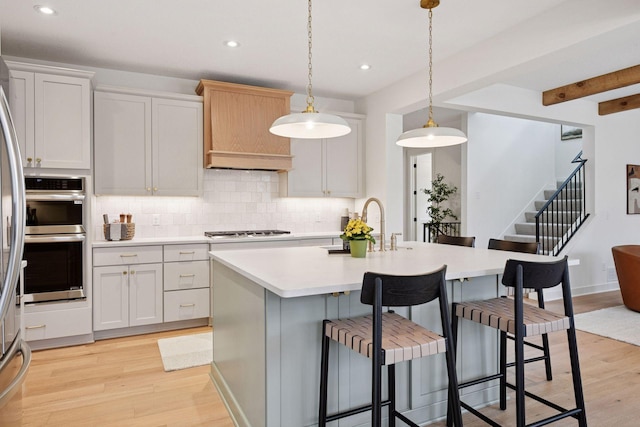 kitchen featuring light wood finished floors, stainless steel appliances, light countertops, a sink, and tasteful backsplash
