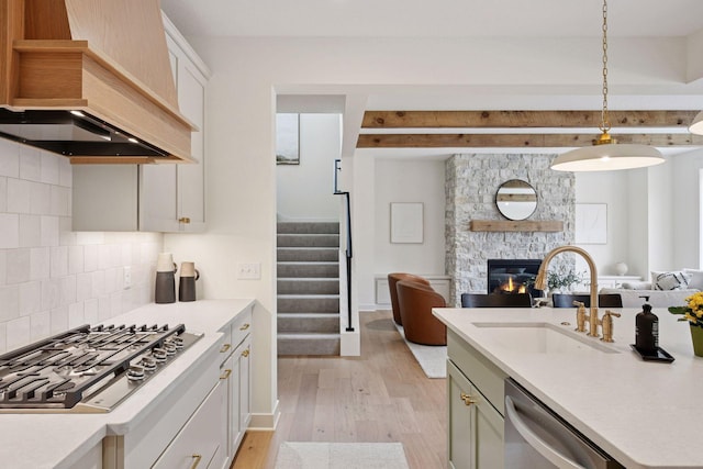 kitchen featuring a sink, light wood-type flooring, open floor plan, appliances with stainless steel finishes, and premium range hood